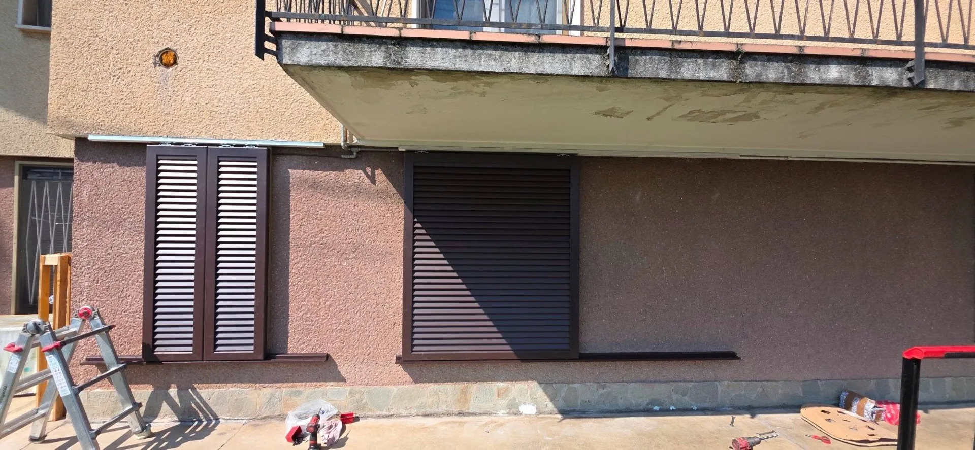 Persiane a lamelle scure sulla facciata di una casa a Brescia, accanto a una seconda finestra schermata.