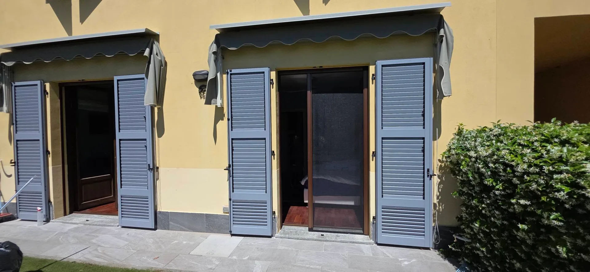 Due porte-finestre con persiane a lamelle grigio-azzurre aperte sulla facciata di una casa a Como.