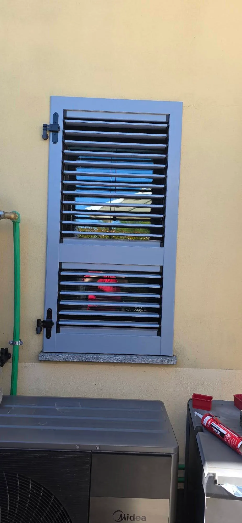 Persiana a lamelle grigio-azzurre davanti a una finestra su parete chiara a Como.