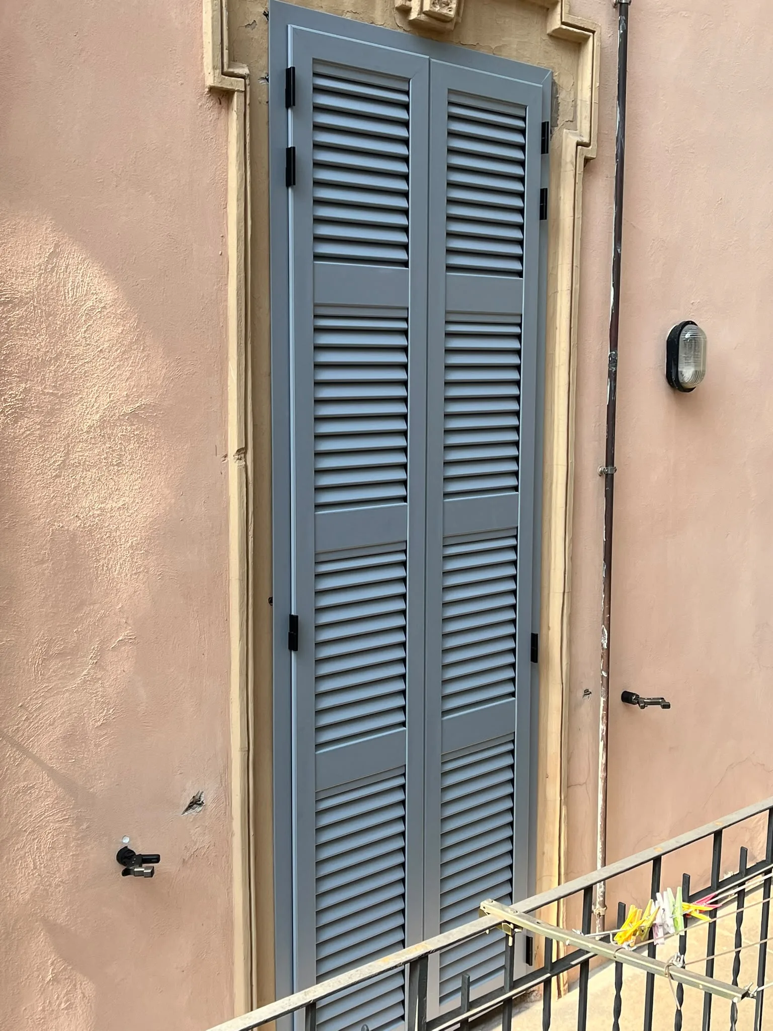 Persiane grigio-azzurre a lamelle chiuse viste di lato su una parete rosa a Milano.