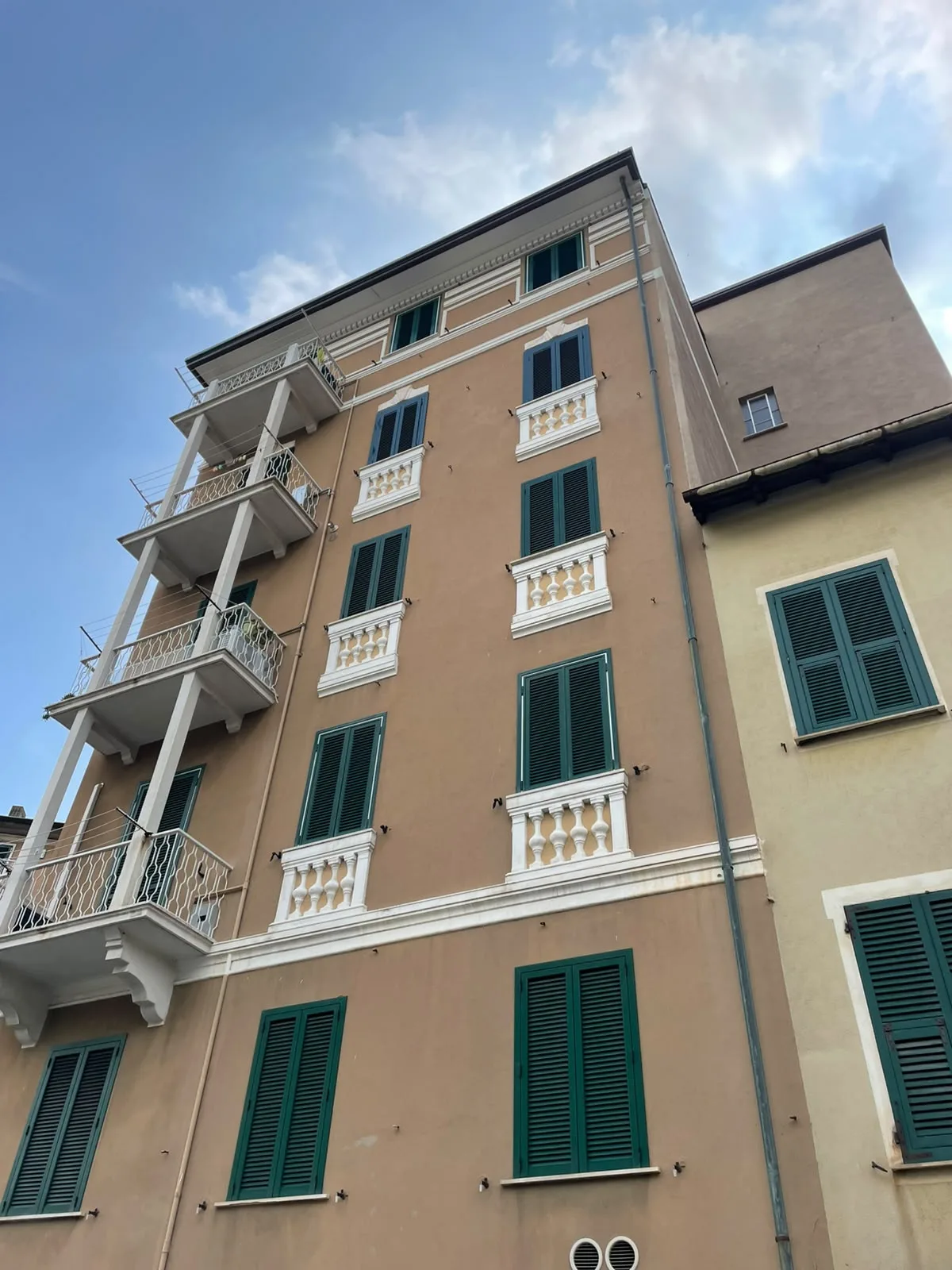Facciata a più piani con persiane verdi a lamelle sulle finestre di un edificio a Milano.