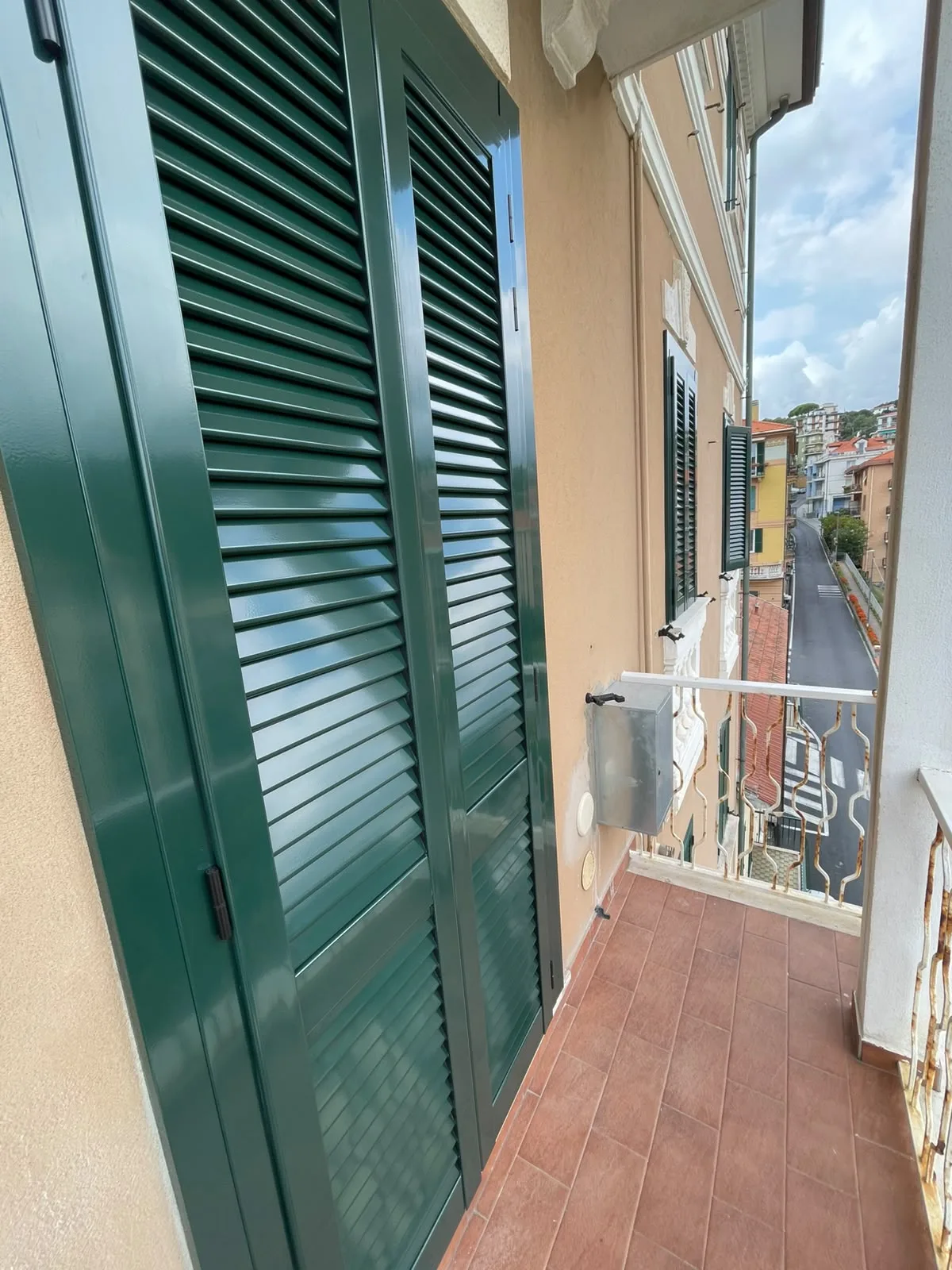 Persiane verdi a lamelle viste da un balcone, con altre finestre e la strada sullo sfondo a Milano.