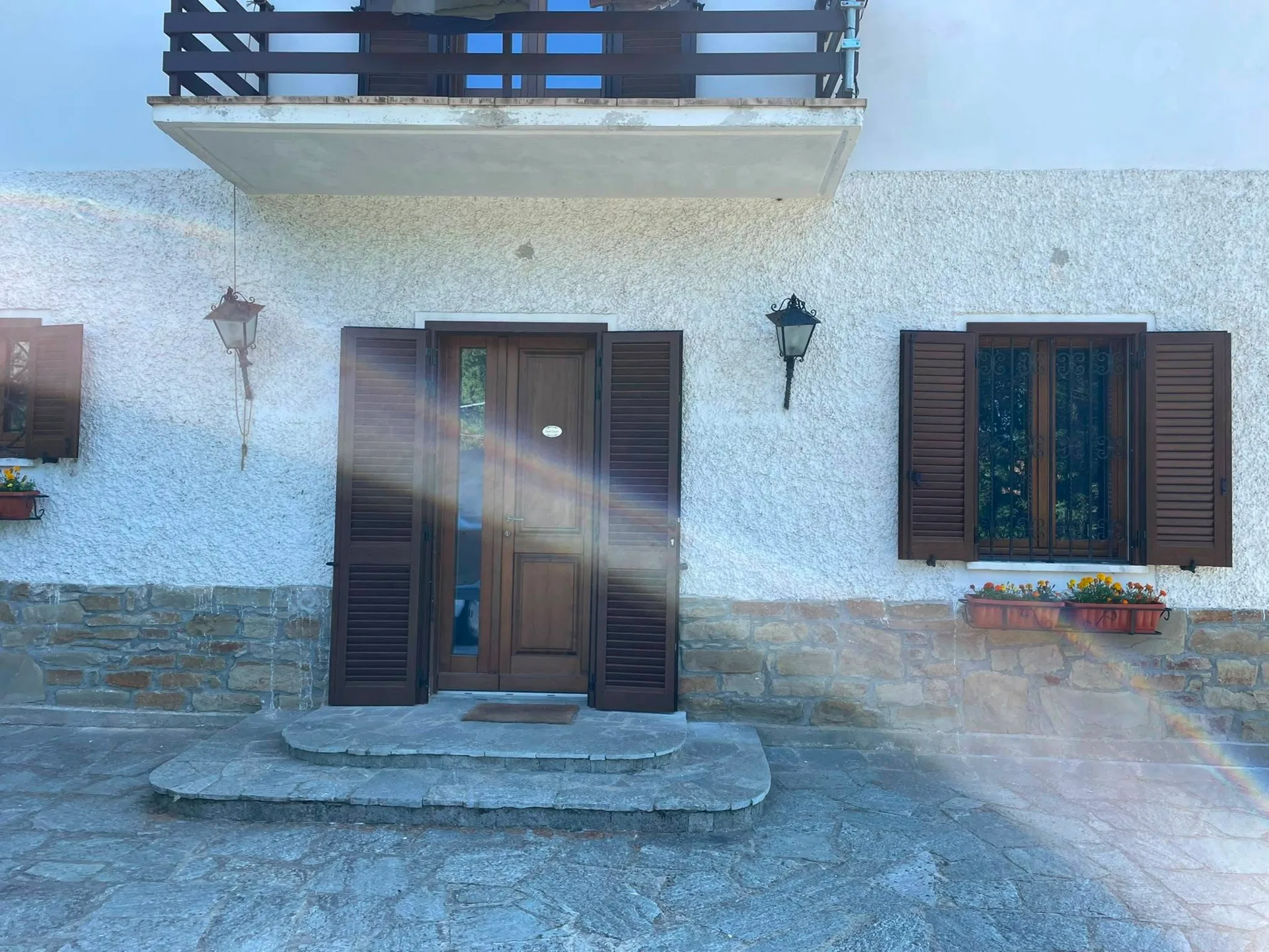 Ingresso e finestra con persiane marroni aperte su una facciata chiara con basamento in pietra in provincia di Monza e Brianza.