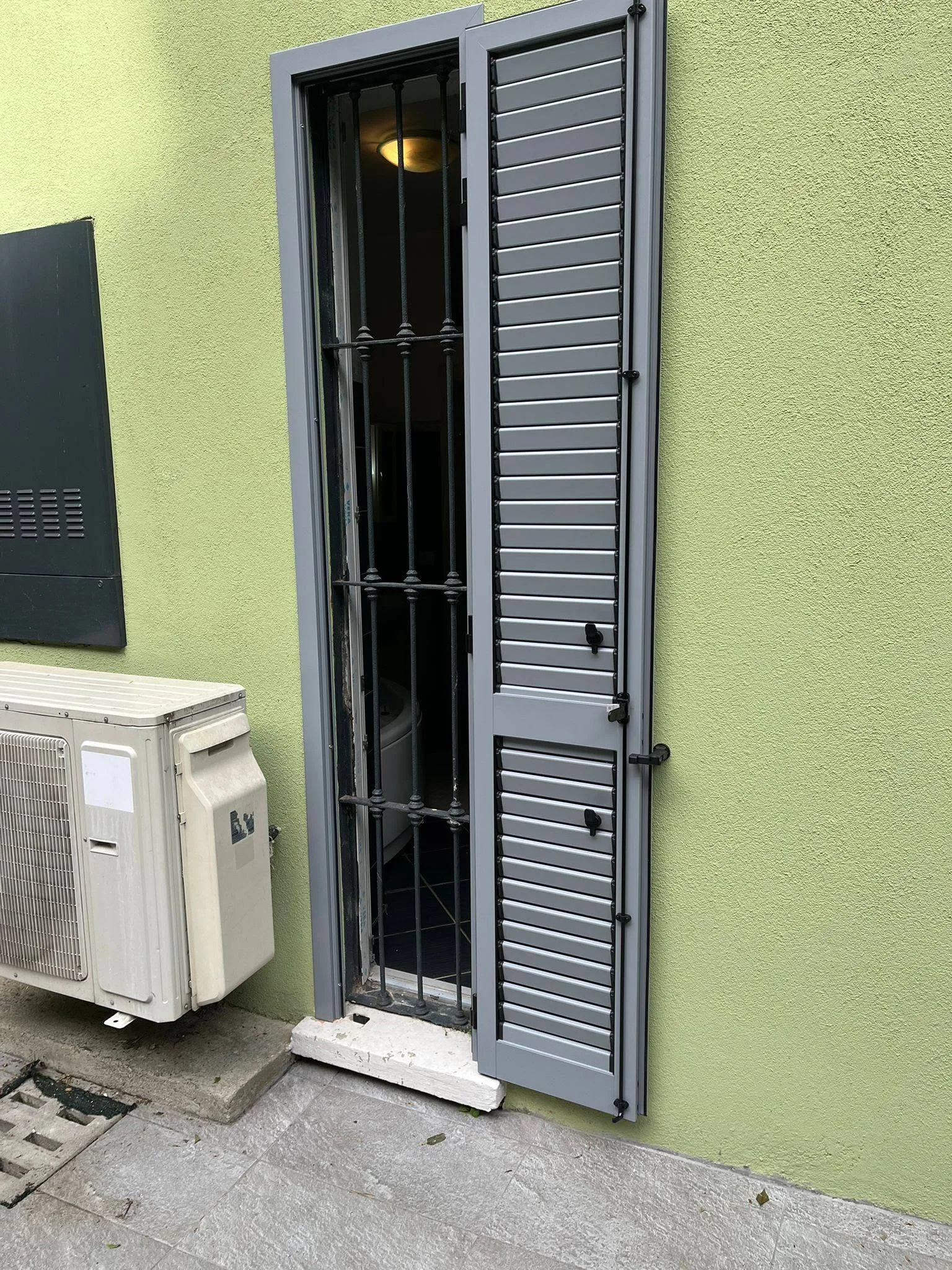 Dettaglio di una persiana grigia a lamelle aperta accanto a una porta-finestra con inferriata a Varese.