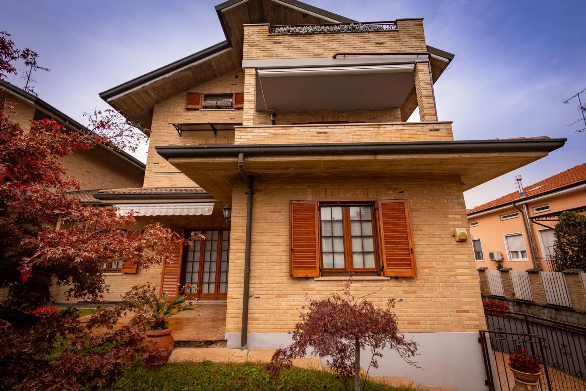 Facciata di una casa in mattoni chiari con persiane marroni alle finestre e balcone superiore a Verona.